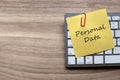 Top view of computer keyboard and yellow memo note with paper clip written with Personal Data on wooden background with copy space