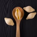 Top view of conchiglie pasta shells on black wooden table with spoon