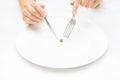 Female hands holding a knife and a fork over a small pea on a large white plate. Royalty Free Stock Photo