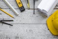 Top view construction tools such as a yellow hard hat, spirit level, measuring tape, folding ruler arrayed against a wooden plank