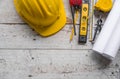 Top view construction tools such as a yellow hard hat, spirit level, measuring tape, folding ruler arrayed against a wooden plank