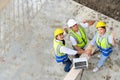 Top view of contractors, engineers and formats team in safety vests with helmets working with laptops, standing on under- Royalty Free Stock Photo