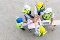 Top view of contractors, engineers and formats team in safety vests with helmets working with laptops, standing on under- Royalty Free Stock Photo