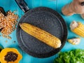 top view of corn cob in pan with corn seeds black pepper seeds cut corn and lettuce around on blue background Royalty Free Stock Photo