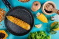 top view of corn cob in pan with corn seeds black pepper seeds cut corn salt lemon and lettuce around on blue background Royalty Free Stock Photo