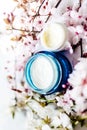 Top view of cosmetic cream and concealer eyes creams with pink cherry flowers in a blue glass jar. Hygienic skincare lotion Royalty Free Stock Photo