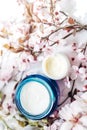 Top view of cosmetic cream and concealer eyes creams with pink cherry flowers in a blue glass jar. Hygienic skincare lotion Royalty Free Stock Photo