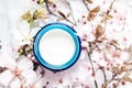 Top view of cosmetic cream with pink cherry flowers in a blue glass jar. Hygienic skincare lotion product