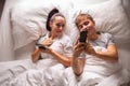 Top view of a couple sharing interesting and funny things on their mobile phones while lying in white bedding before sleep