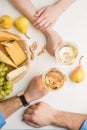 Top view of couple with wine glasses, different types of cheese, pears, grapes and almond on white