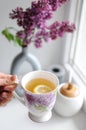 Top view concept of woman hand holding a cup of tea. Lilac flowers on background Royalty Free Stock Photo