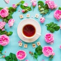 Top view creative layout with Tea time lettering with wooden blocks, cup of hot tea and fresh pink tea rose flowers, buds, petals,