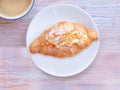 Top view, Croissant with cream and almonds on white plate and coffee cup over wooden table.