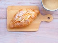 Top view, Croissant with cream and almonds on wooden plate and coffee cup over wooden table.