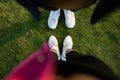 Top view of crop anonymous couple of tourists in sneakers standing on ground with green grass