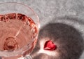 Top view of crystal glass of rose sparkling wine or champagne and red glass heart on grey stone background in hard light