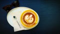 Top view of cup of art cappuccino or latte coffee putting in tray with tea spoon, napkin and brown sunglasses on wooden table Royalty Free Stock Photo