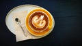 Top view of cup of art cappuccino or latte coffee putting in tray with tea spoon and napkin on dark blue wooden background. Royalty Free Stock Photo