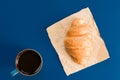 Top view of cup of black coffe and croissant on craft paper on blue background with copy space. Morning breakfast in french style Royalty Free Stock Photo