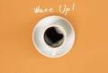 Top view of cup of black coffee and Wake Up lettering on orange background