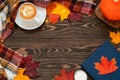 Top view of a cup of coffee, book, candle, plaid scarf, fairy lights, pumpkin, red, orange and yellow leaves on the wooden backgro
