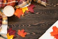 Top view of a cup of coffee, book, plaid scarf, fairy lights, yellow, orange and res leaves on the wooden table.