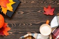 Top view of a cup of coffee, book, plaid scarf, pumpkin and colourful leaves on the wooden table. Slow living concept.