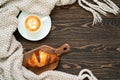 Top view of a cup of coffee, fresh croissant and knitted plaid on the wooden table. Cozy and warm flat lay with copy space. Royalty Free Stock Photo