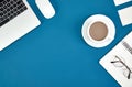 Top view of a cup of coffee, laptop, notebook, and glasses on a blue surface Royalty Free Stock Photo