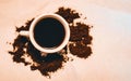 Top view of a cup of coffee and scattered ground coffee on the light surface