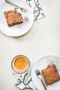 Top view of a cup of coffee and two dessert plates with brownie cake over white rustic background