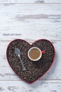 Top view of a cup of espresso in a red cup on top of freshly roasted coffee beans in a heart shaped tray on textured white wooden Royalty Free Stock Photo