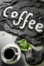 Top view on cup of hot black coffee with green leaves and text word hand written in english `coffee` in milled coffee texture