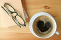 Top View of a Cup of hot coffee with heart shape foam on wooden table with some books and glasses Royalty Free Stock Photo