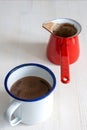 Top view of cup of rustic chocolate and red saucepan, on white wooden background in vertica