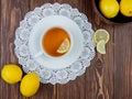top view of cup of tea with lemon slice in it on paper doily and lemons on wooden background