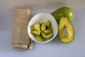 Top view of cut-up pieces of avocado pieces in a bowl and halved avocados on a kitchen table