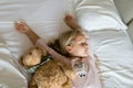 Top view of cute blonde little girl in pajamas lying in white bed with teddy bear, awaking early in the morning before going to Royalty Free Stock Photo