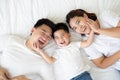 Top view of cute little boy and his asian parents looking at camera and smiling while lying on the white bed at home, Happy Family Royalty Free Stock Photo