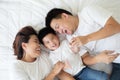 Top view of cute little boy and his asian parents looking at camera and smiling while lying on the white bed at home. Royalty Free Stock Photo