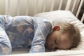 Top view Cute little 2-3 years preschool baby boy kid sleeping sweetly in white crib during lunch rest time in blue pajama with Royalty Free Stock Photo