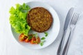 Top view of cutlets with vegetable mix, salads, tomatoes, knife, and fork on white table