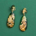 Top view of dangle earrings made of epoxy resin with golden foil inside isolated over green background