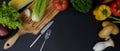 Dark kitchen table with assorted fresh vegetables, chopping board, silverware and copy space Royalty Free Stock Photo