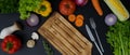 Dark kitchen table with assorted fresh vegetables, chopping board and silverware Royalty Free Stock Photo