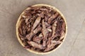 Top view on dehydrated homemade pet beef lungs chips in straw pot on stone background. Dog and cat chewy jerky and treats.