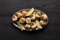 Top view of delicious cooked escargots with lemon on black wooden table.