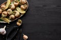 Top view of delicious cooked escargots with lemon and tweezers on black wooden table.