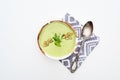 Top view of delicious creamy green vegetable soup with sprouts and pumpkin seeds on napkin with spoon isolated on white.