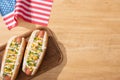 Top view of delicious hot dogs with corn, green onion and mayonnaise on board near american flag on wooden table. Royalty Free Stock Photo